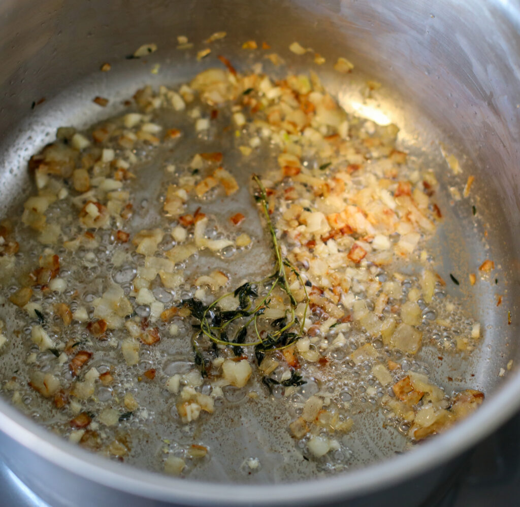 shallots and thyme cooking in bacon fat in stainless steel pot